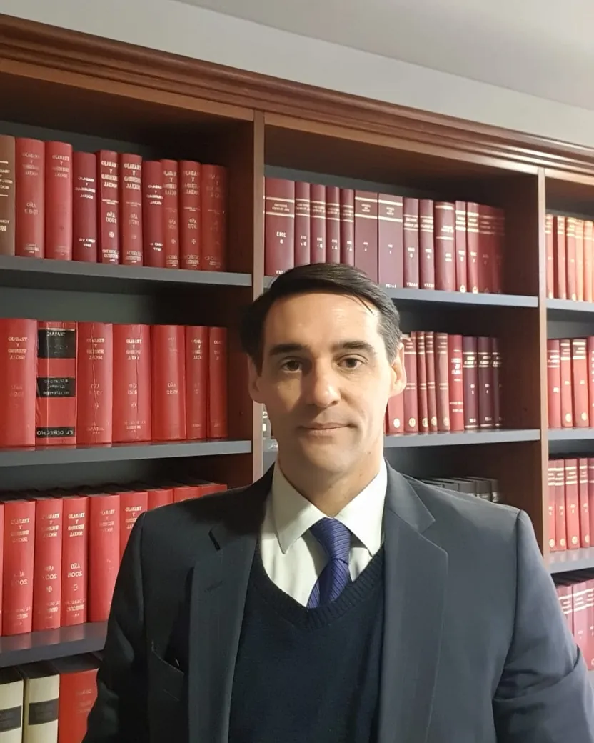 El Dr. Jorge Alberto Narváez de traje, en su estudio, frente a una biblioteca de libros de derecho